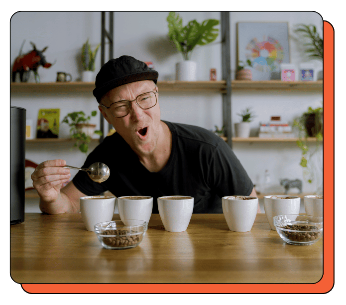 Owner Michael Craig tasting coffee in a cozy cupping table setting with shelves and plants. Michael loves coffee!