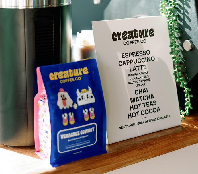Blue Creature Coffee Packaging Bag with cartoon characters and a white coffee catering menu board for Creature Coffee Co.