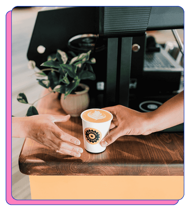 Barista handing a custom printed compostable coffee cup to another person with a coffee machine in the background at an event. Excellent latte art from a barista on a mobile coffee cart.