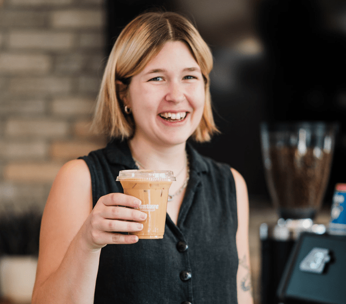 Woman holding a coffee cup in a casual setting, smiling, enjoying her latte from Creature Coffee Catering