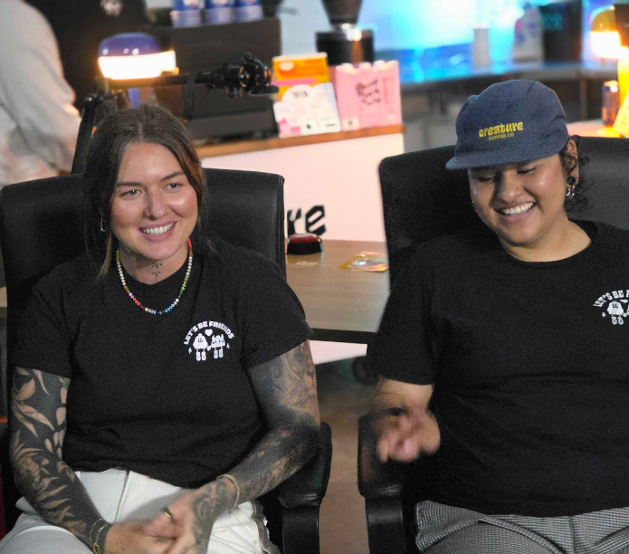 Two happy baristas sitting in chairs with a blurred background at a latte art throwdown in Seattle for Creature Coffee and Outyouth