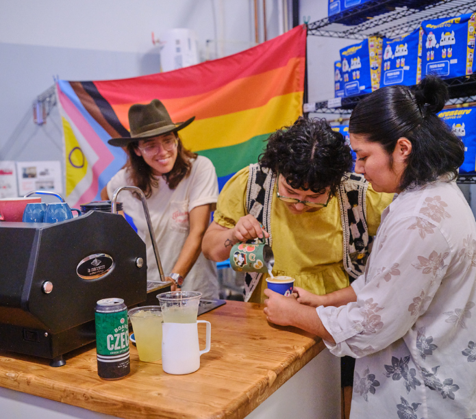 Three barista friends at a counter with a rainbow flag in the background