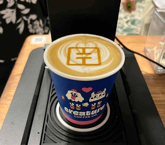 Coffee cup with latte art and 'Creature Coffee Co' branding on a mobile espresso cart.