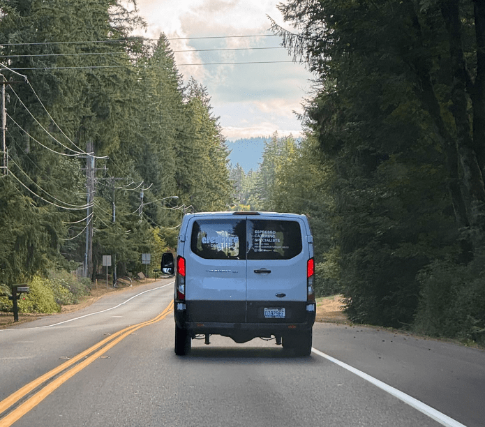 Creature Coffee van driving on a road surrounded by trees