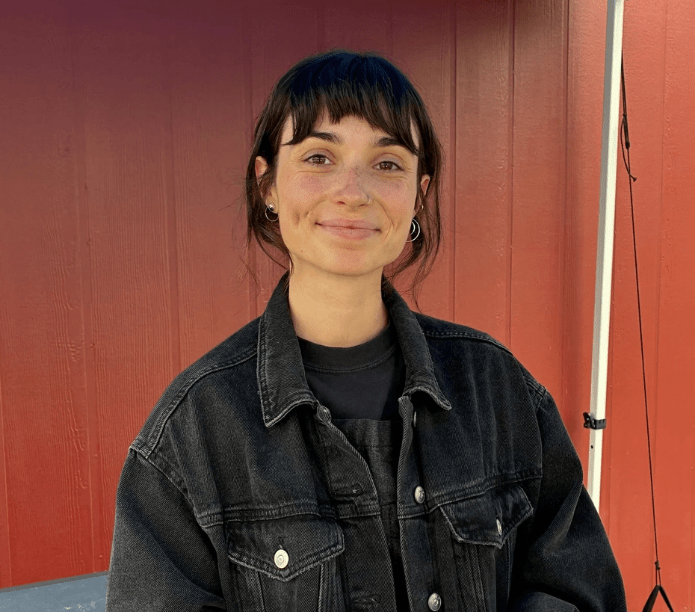 Creature Coffee barista wearing a black denim jacket in front of a red wall