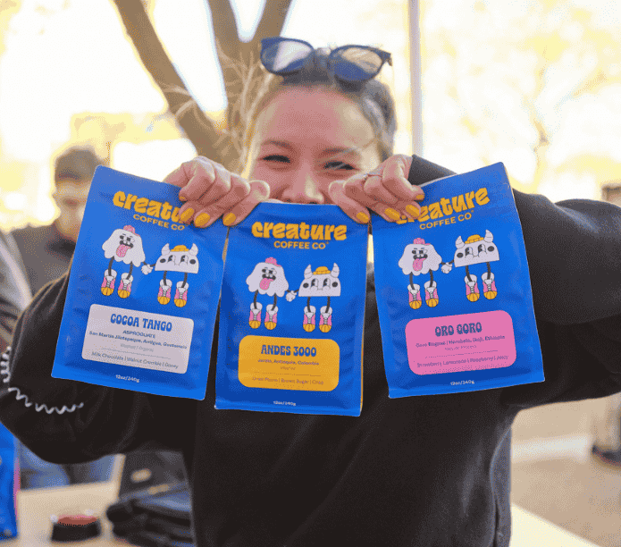 Coffee Creature holding three packages of 'creature Coffee Co' coffee
