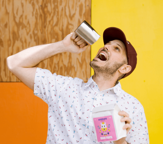 Ben holding a mug and a pink container with a cartoon character against a colorful background