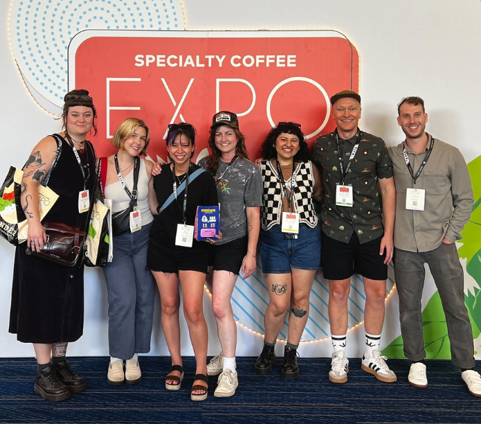Group of people posing in front of a Specialty Coffee Expo sign.