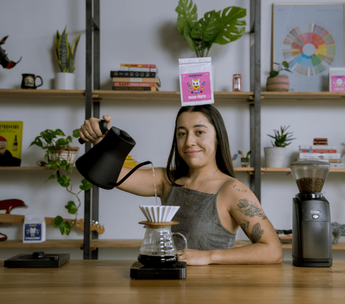 Person making coffee in a home kitchen setting with shelves and plants in the background