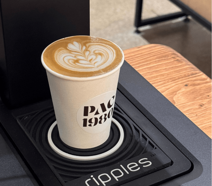 Cappuccino in a white cup with 'Pac 1980' custom printed logo on a black coaster with 'ripples' branding.