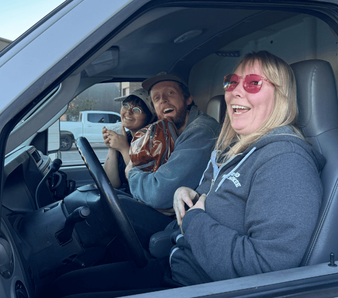 Three baristas in a Creature Coffee truck, all of whom are smiling and looking out the window.