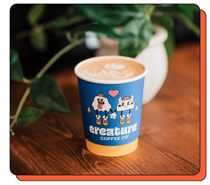 Blue paper cup with a cartoon design on a wooden table, containing a latte.