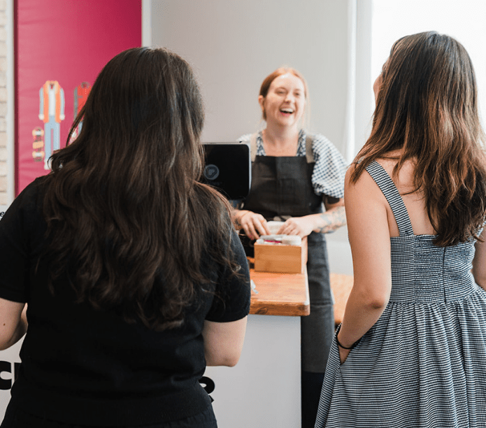 Two women standing at a mobile espresso bar in the office with a smiling staff member behind them.