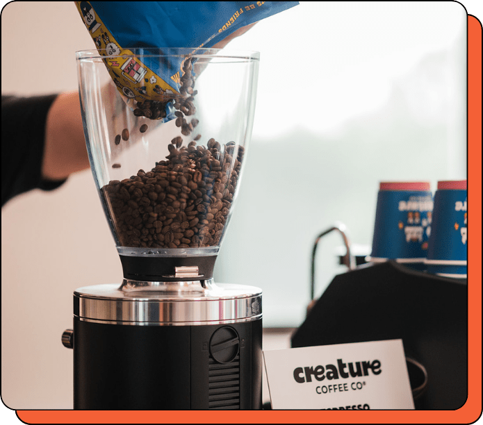 Coffee grinder with coffee beans being poured into it, featuring 'creature Coffee Co.' branding.