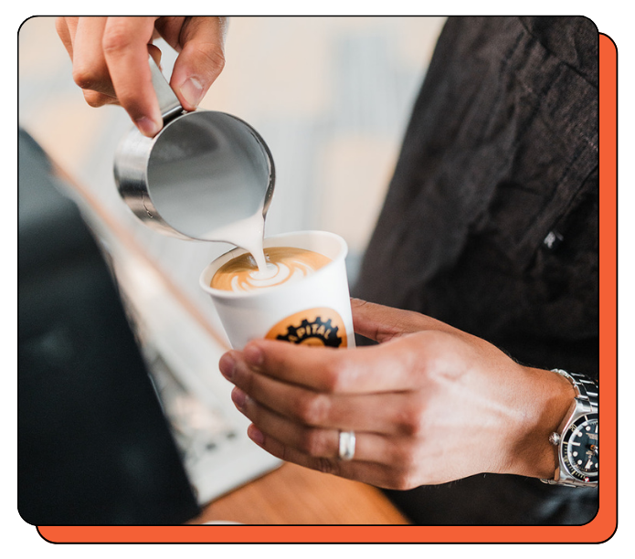 Person pouring milk into a coffee cup with a visible brand logo. Custom-branded mobile coffee cart from Creature Coffee. Silky latte art skills from the best baristas in Austin and Seattle.