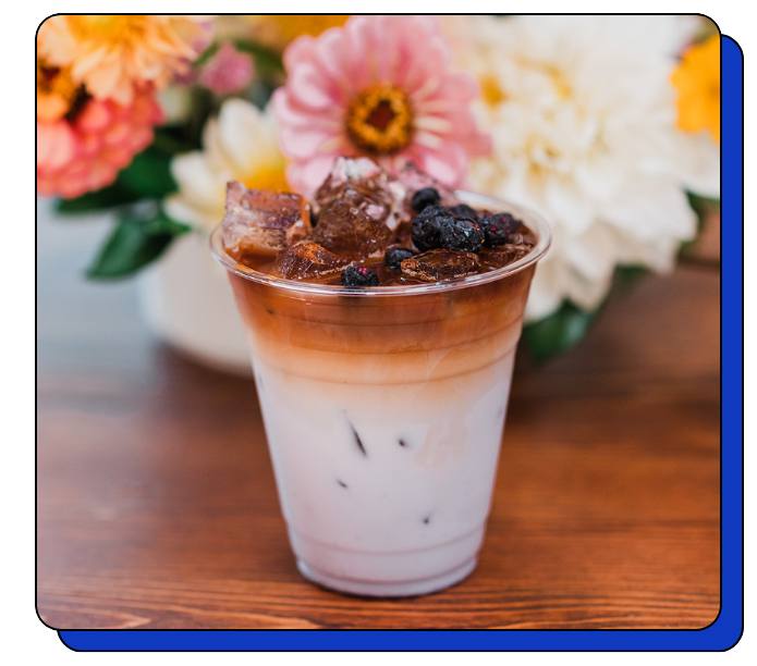 Signature Latte Drink with chocolate topping and berries on a wooden mobile coffee cart with flowers in the background