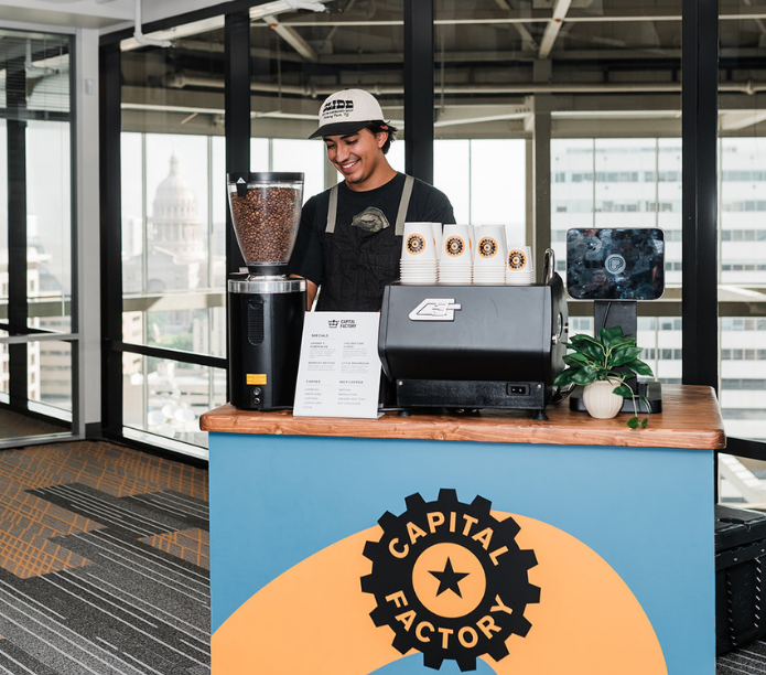 Barista behind a coffee catering mobile espresso bar with coffee equipment and custom cups, custom-branded cart with'Capital Factory' branding.