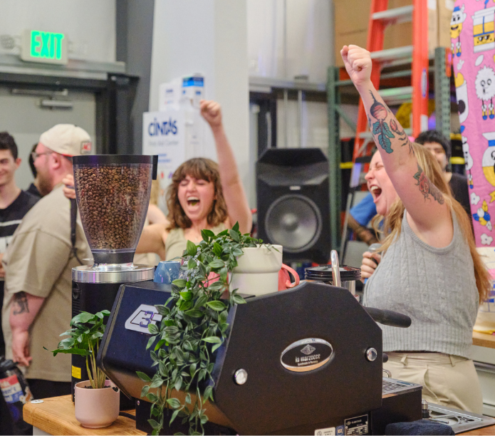 People celebrating in a latte art throwdown at Creature Coffee Austin with a coffee grinder and plants.