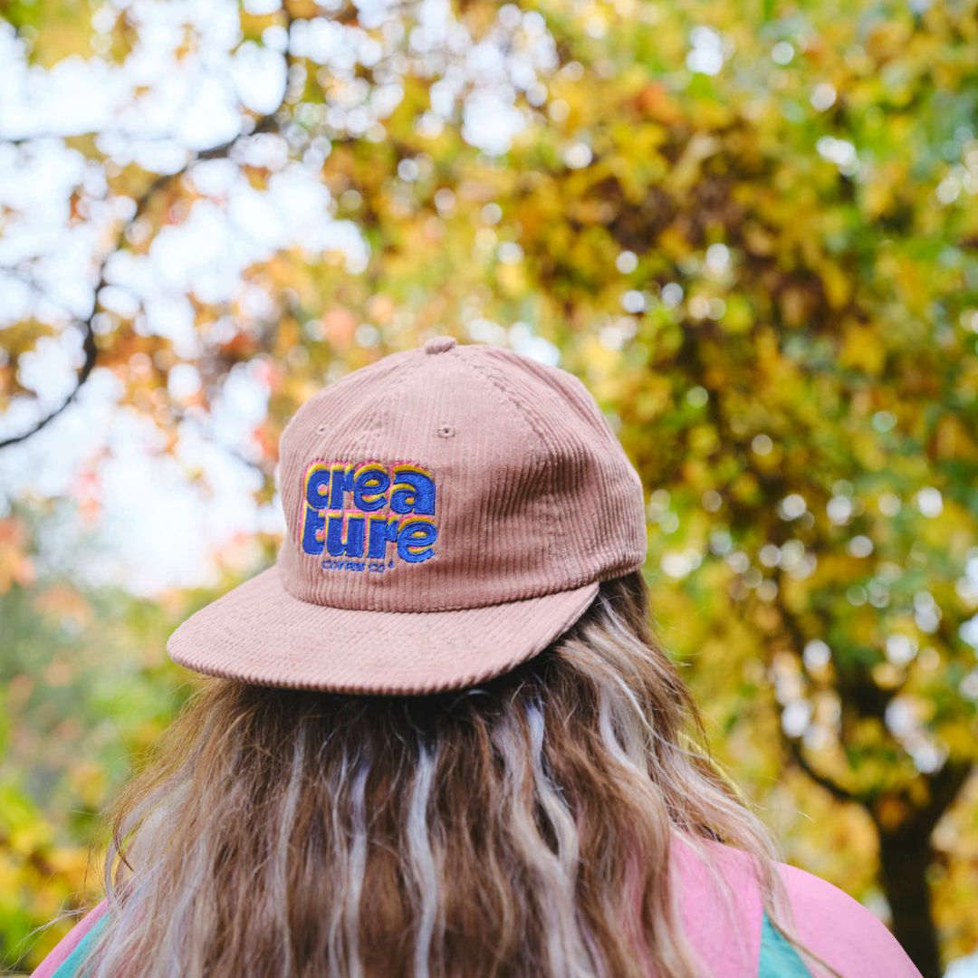 Person wearing a cap with 'creature coffee' logo in an autumn setting