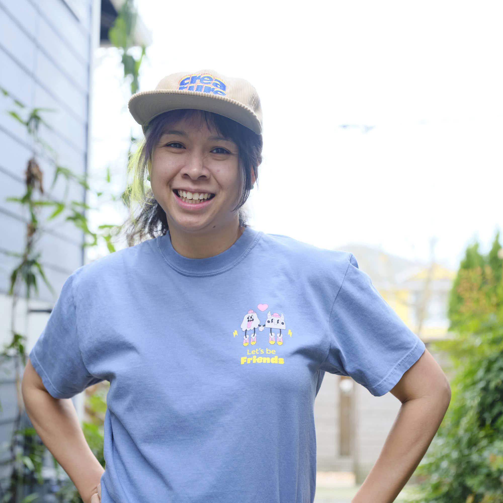 Person wearing a blue creature coffee t-shirt with a graphic design and a cap outdoors.