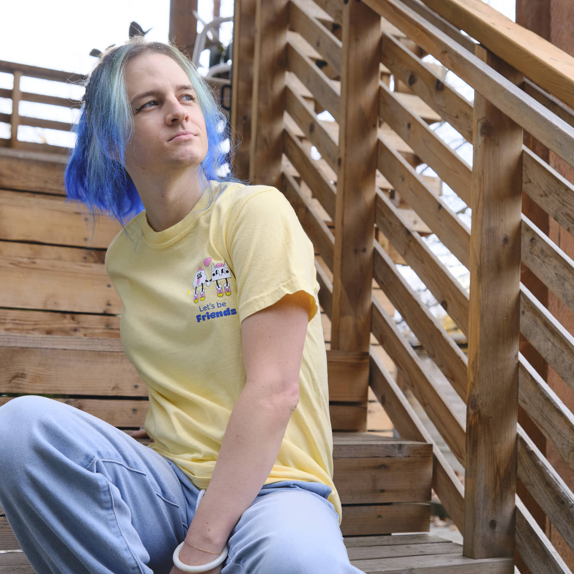 Person wearing a yellow creature coffee t-shirt with a graphic design, sitting on wooden steps.