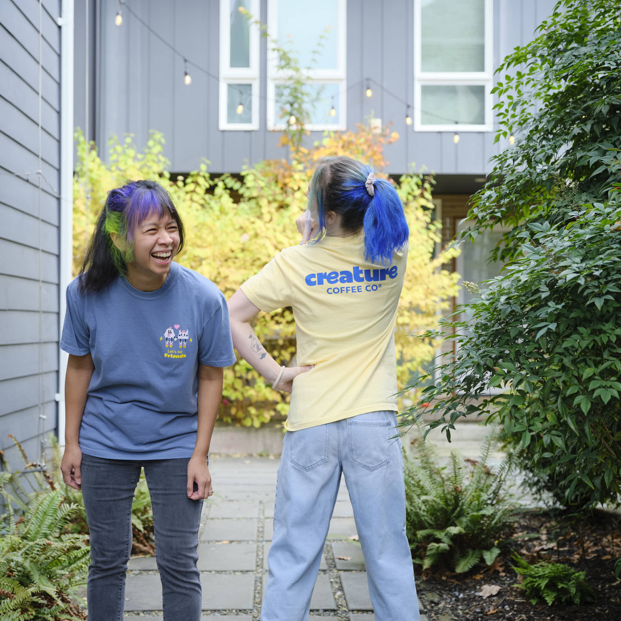 Two people standing outdoors with one wearing a 'creature coffee co.' shirt.