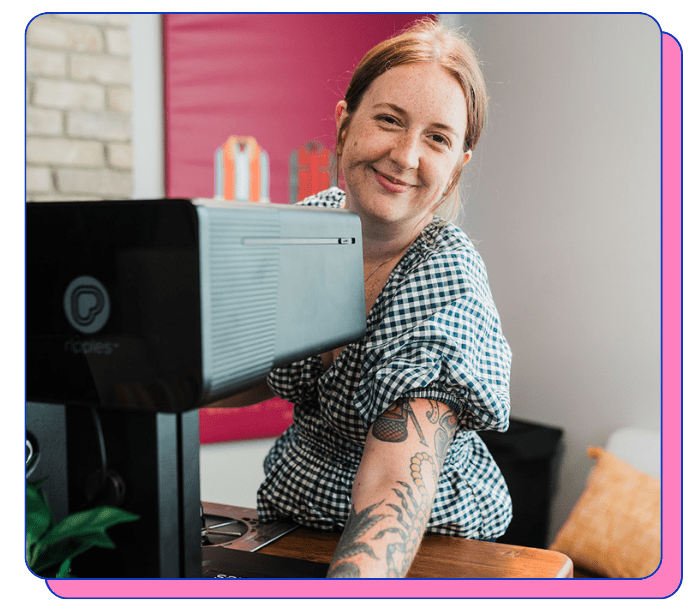 Smiling barista serving a latte with a latte art printer, wearing a checkered shirt and smiling.